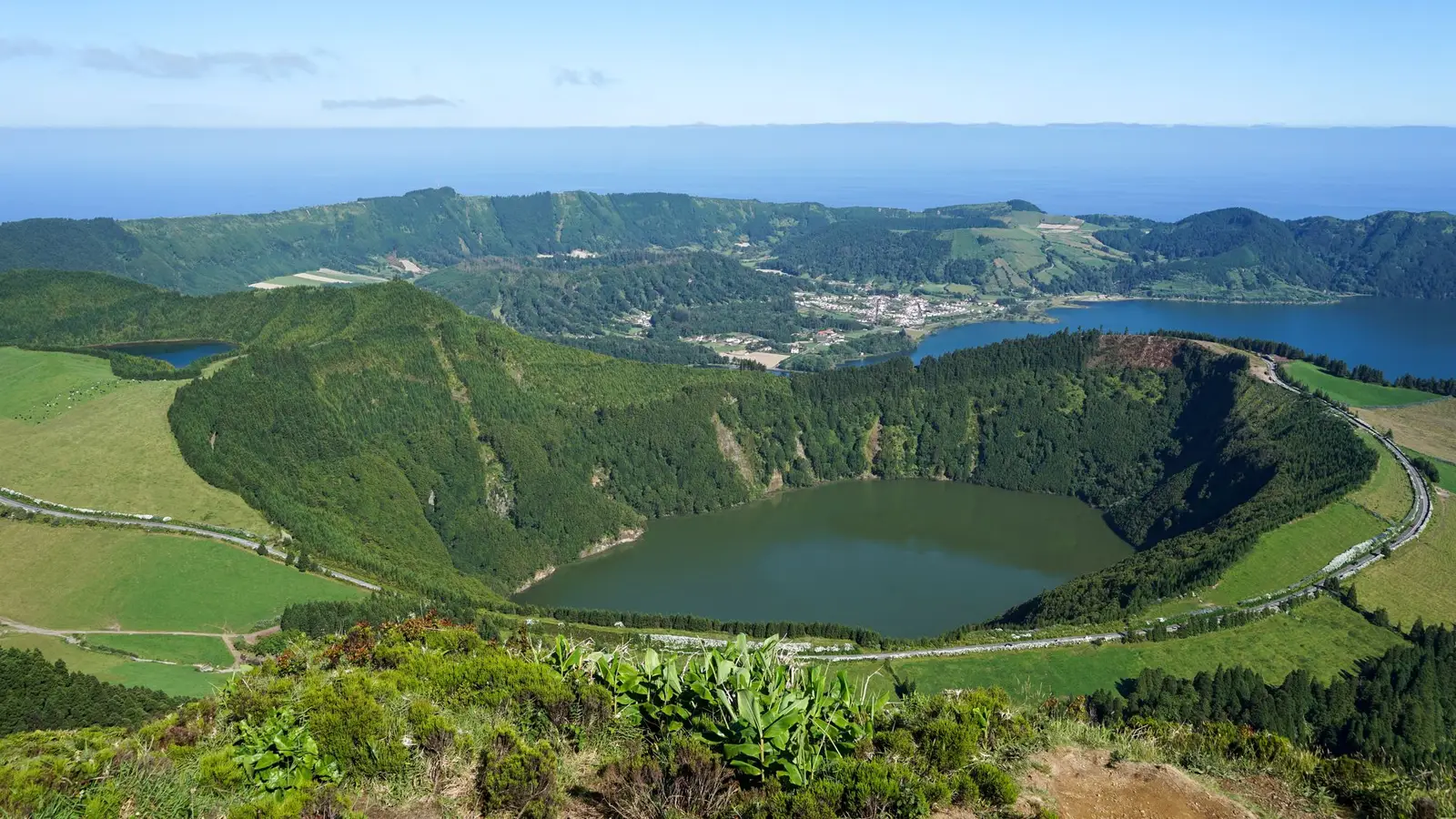 A stunning aerial view of a lush green landscape featuring a crater lake surrounded by hills and valleys.