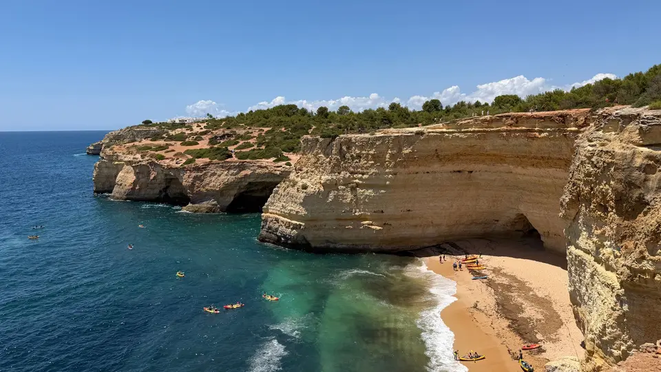 Explore the captivating limestone cliffs and clear waters of Algarve, Portugal, with kayakers enjoying the serene beach setting.