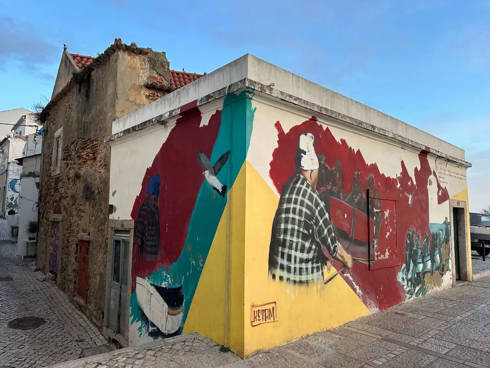 Colorful street art mural on a building corner in Sesimbra, Portugal alley.