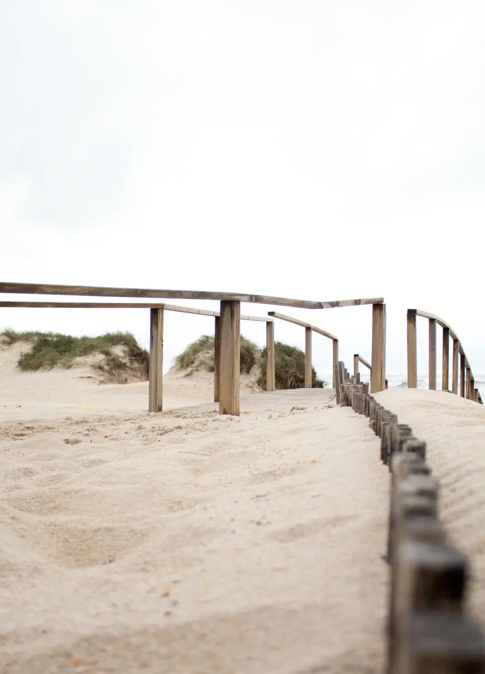 Scenic view of a sandy beach pathway with wooden railings and ocean waves in Aveiro, Portugal.