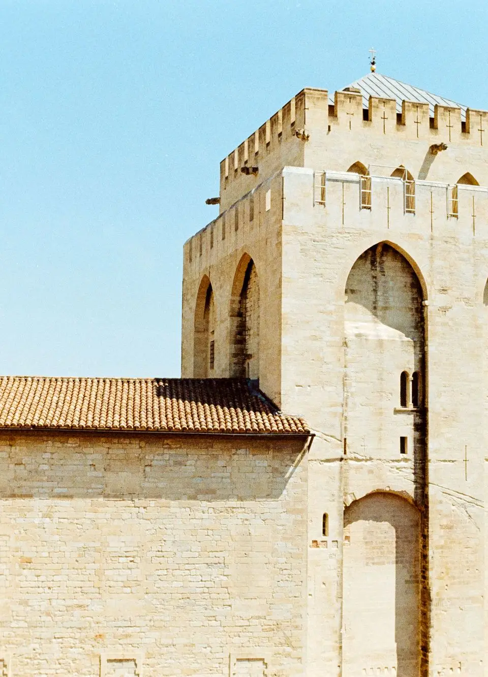Stone facade of the historic Palace of the Popes in Avignon, France, under a clear blue sky.