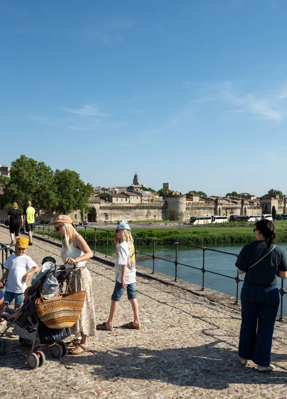 Tourists explore Pont Saint-Bénézet in Avignon, enjoying a sunny day by the Rhône River.