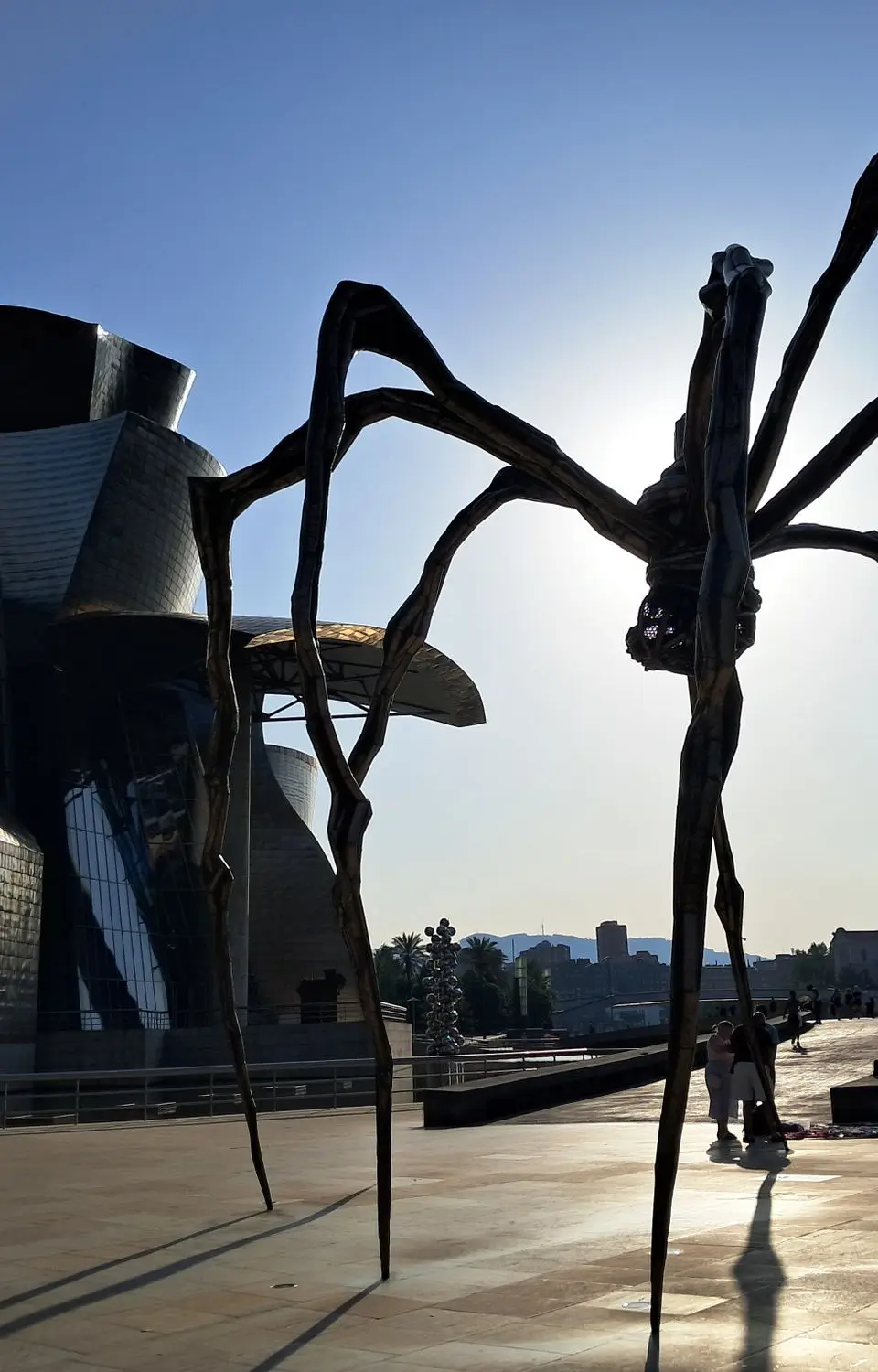 Silhouette view of the Guggenheim Museum Bilbao and Maman sculpture against bright sunlight.
