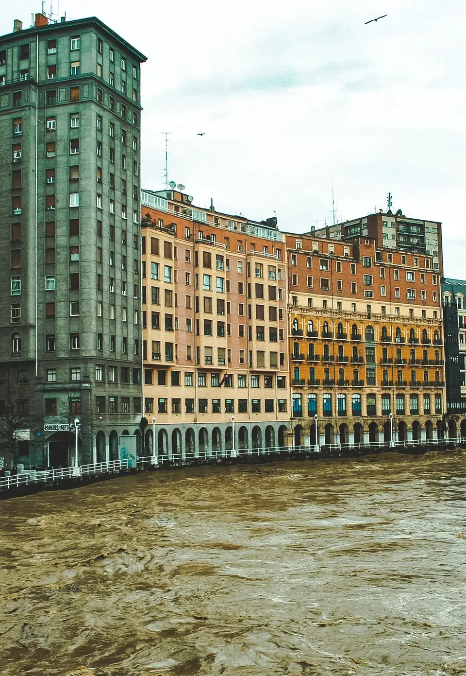Vibrant architecture along the Nervión River in Bilbao, Spain on an overcast day.