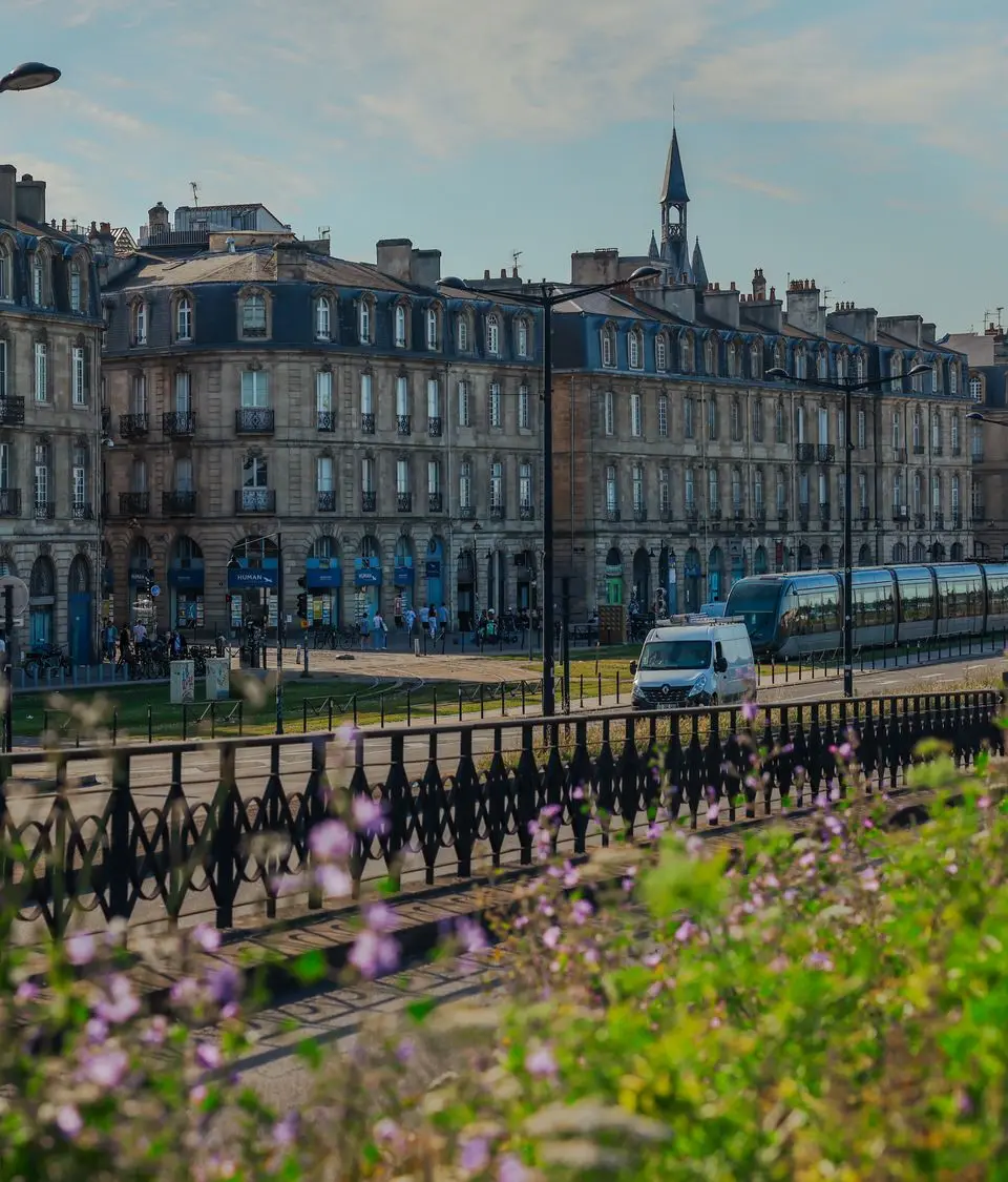 Charming view of historic buildings and tram in Bordeaux, France, with vibrant flowers in foreground.
