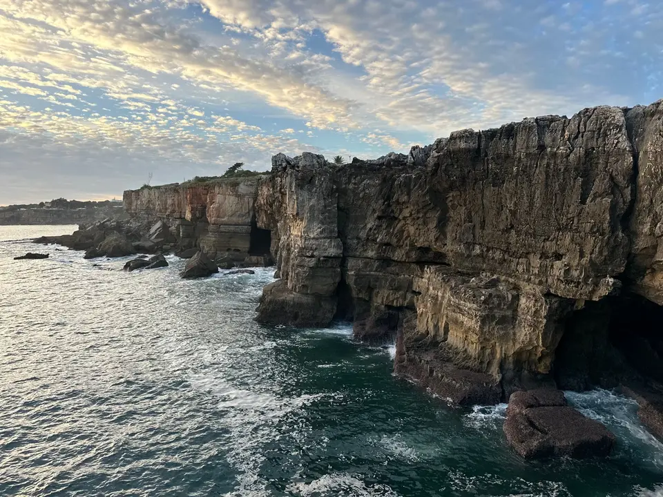 Spectacular view of crashing waves against rugged cliffs in Cascais, Portugal during a beautiful sunset.