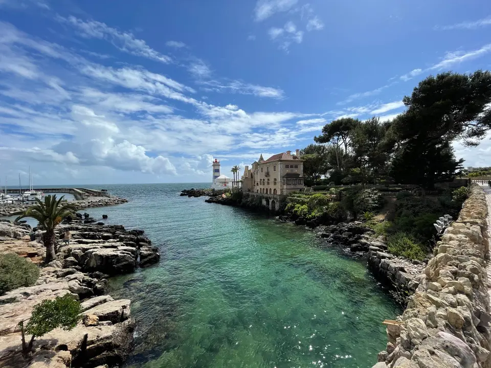 Dramatic view of Santa Marta Lighthouse along with rocky coastline and lush greenery under a bright blue sky.