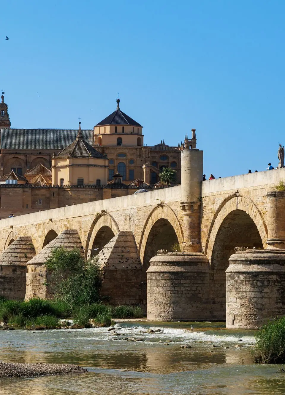 View of the Roman Bridge and Mezquita of Córdoba under a clear blue sky in Andalusia, Spain.