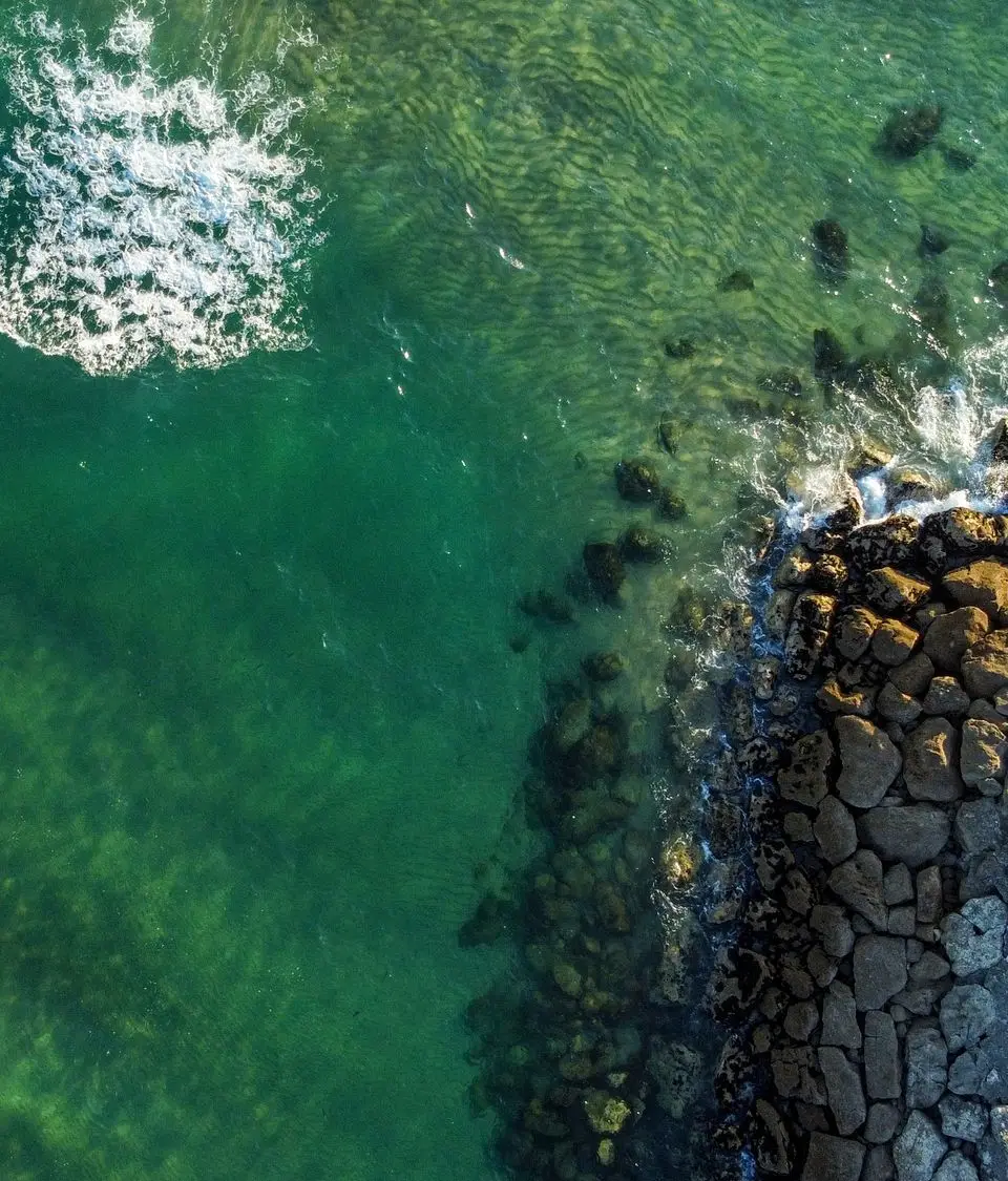 A stunning aerial view of a rocky pier extending into the emerald green sea at Costa da Caparica, Portugal.