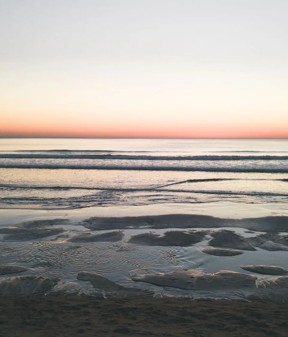 Lone figure on Costa da Caparica beach at sunrise, capturing a serene ocean view.