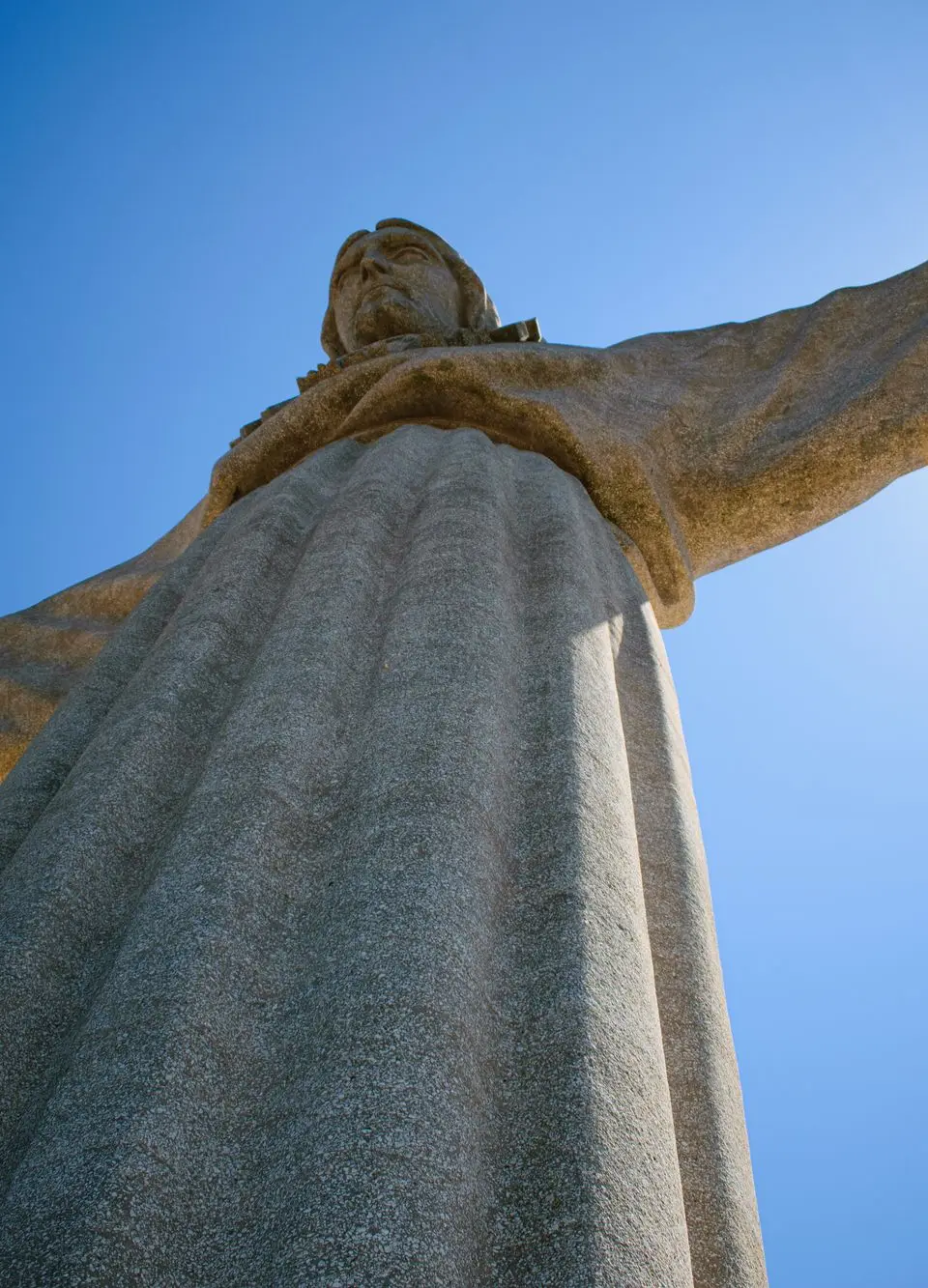 View of the iconic Cristo Rei statue in Almada, Portugal against a clear blue sky.