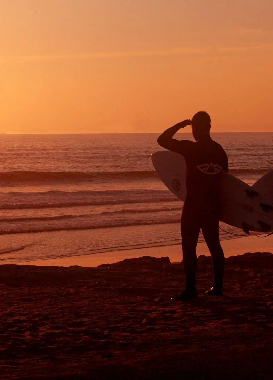 Silhouetted surfers with boards watching the sun set at Costa da Caparica, Portugal.