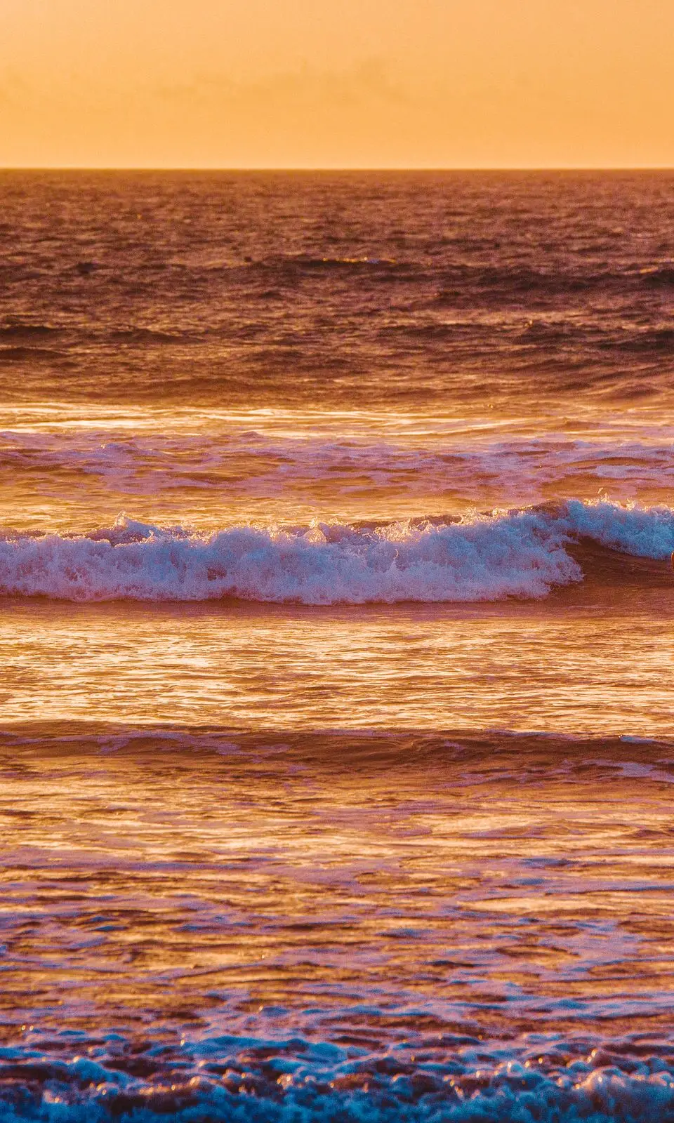 A silhouette of a surfer entering the ocean at sunset on Costa da Caparica beach, Portugal.