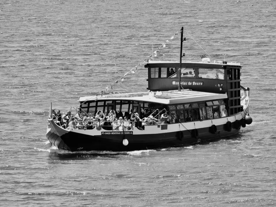 A black and white photo of a tour boat on the Douro River filled with tourists.