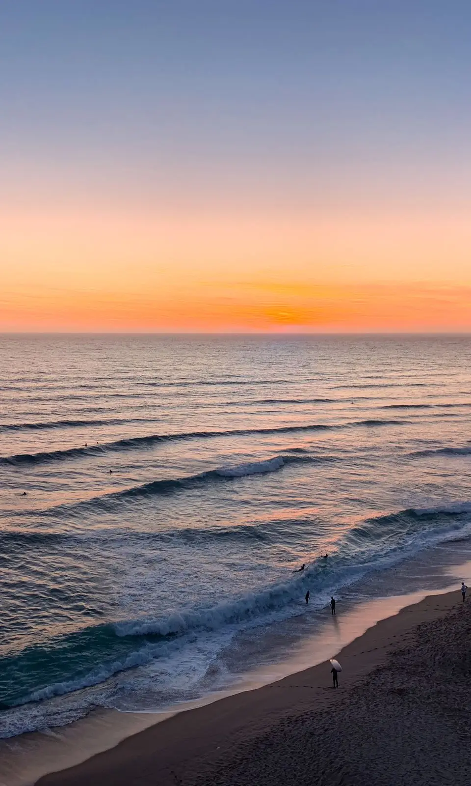 Captivating sunset view over Ericeira Beach, Portugal with gentle waves and sandy shore.