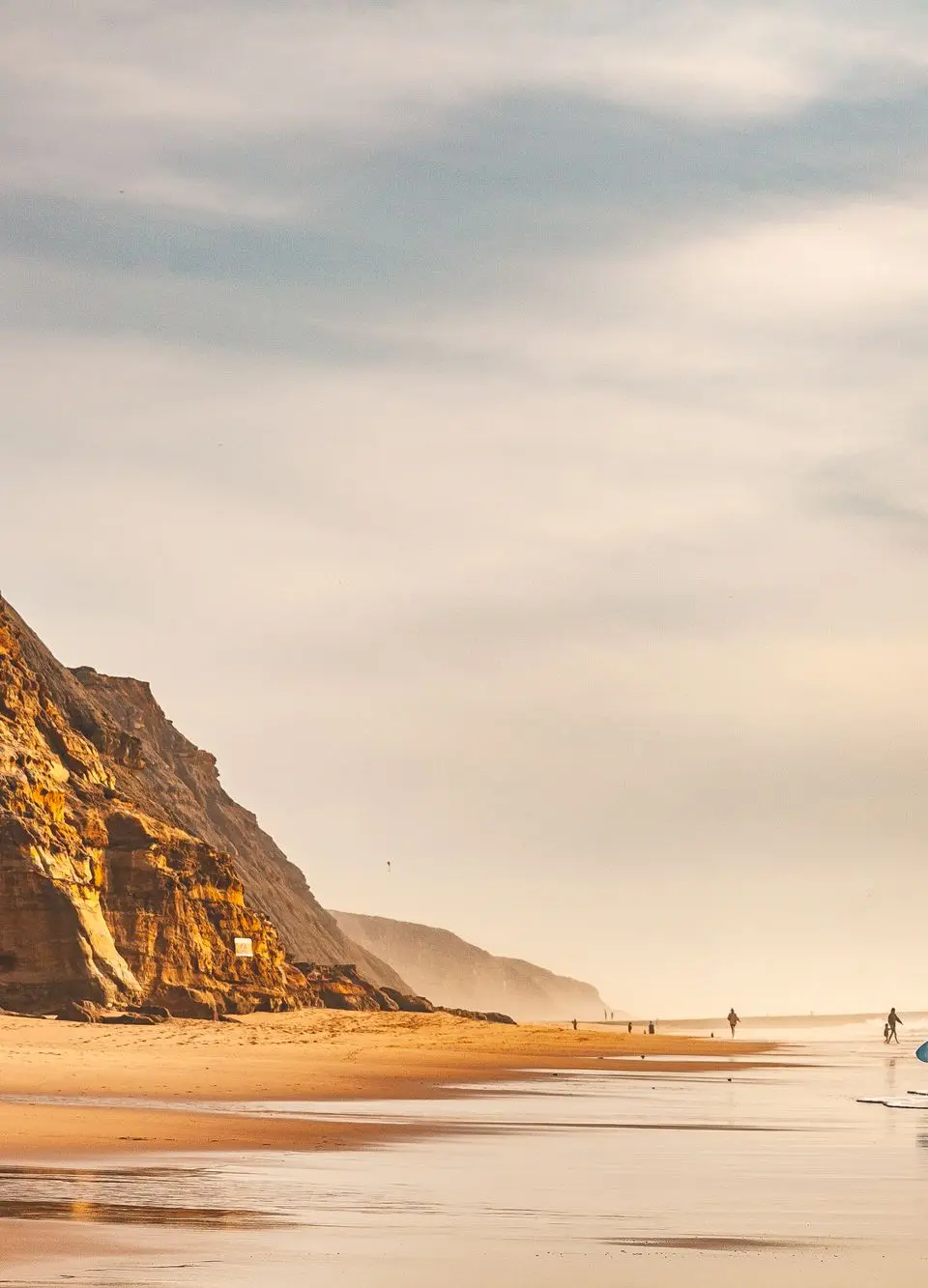 Surfer walking along Ericeira beach with a vibrant sunset and scenic cliffs. Ideal travel destination.
