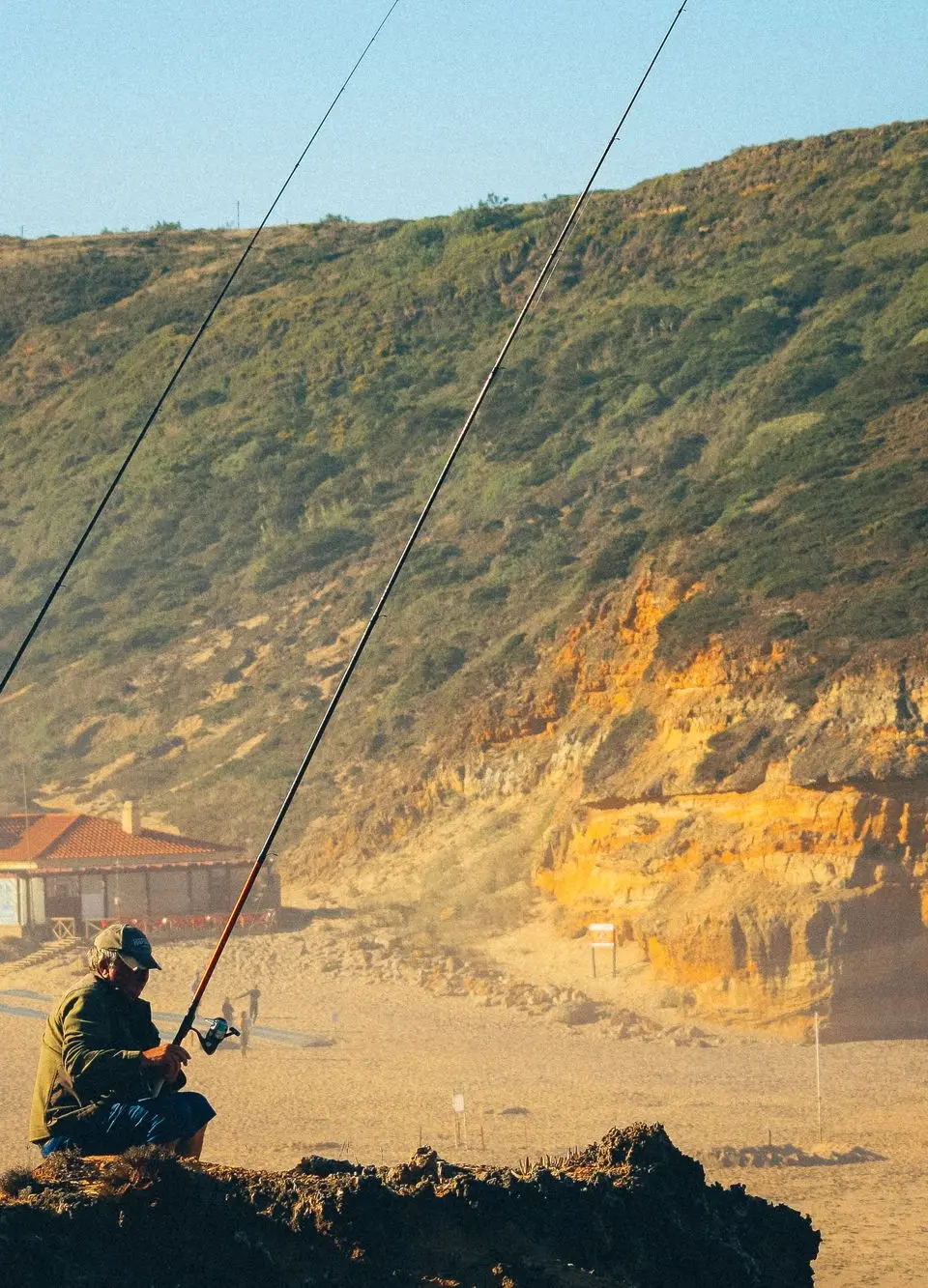 Two fishermen with rods on the scenic Ericeira beach, Portugal, at dusk.