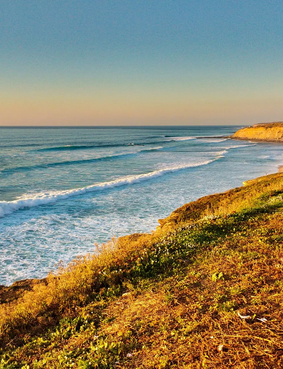 Capture of Ericeira coastline with waves gently crashing against the shore under a clear sky.