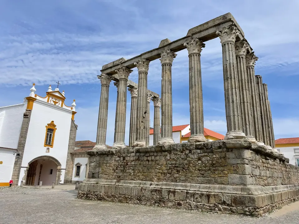 View of the Roman Temple and a Baroque church facade in Évora under a blue sky.