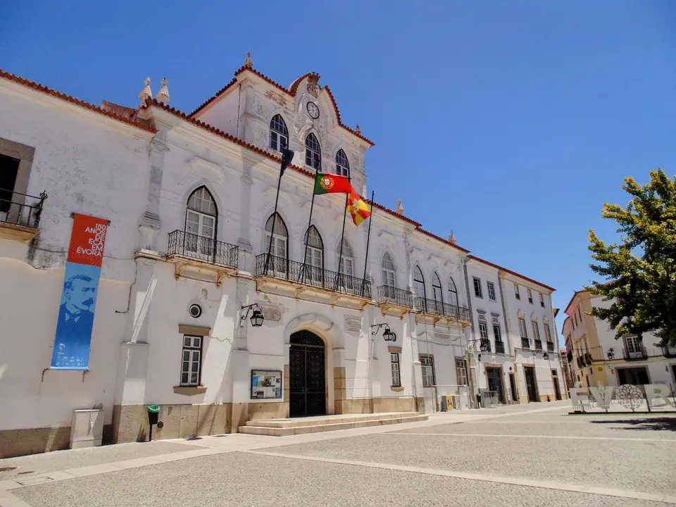 A sunny day view of a historic building in Évora, Portugal, displaying the Portuguese and Spanish flags.