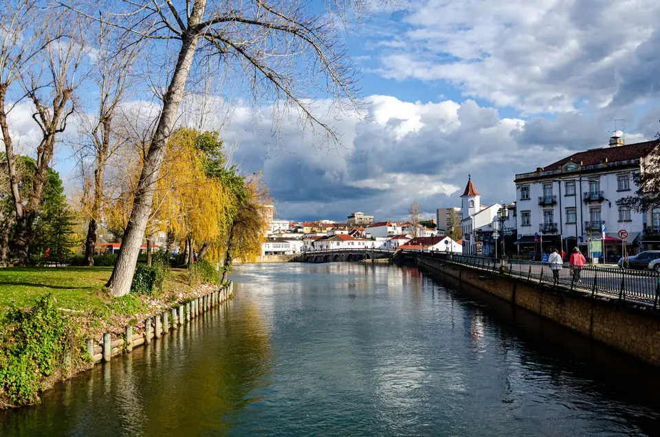 Charming city scene of Tomar with autumn trees along the riverbanks under a dramatic sky.