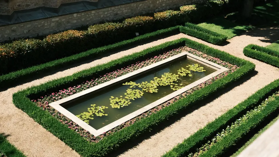A top view of an elegant rectangular pond surrounded by symmetrical hedges and flowers, in bright daylight.