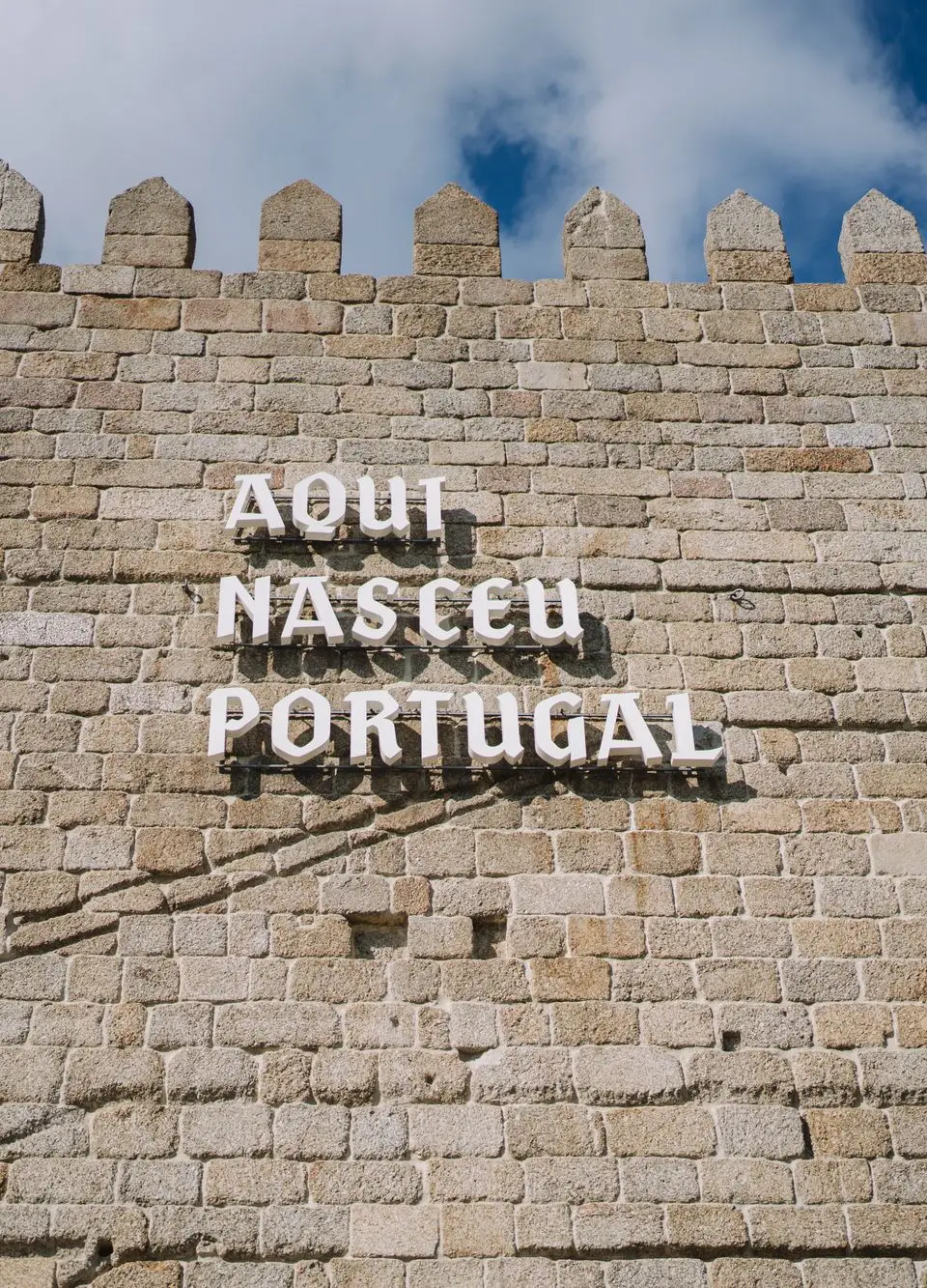 Medieval stone wall with 'Aqui Nasceu Portugal' sign in Guimarães under blue sky.
