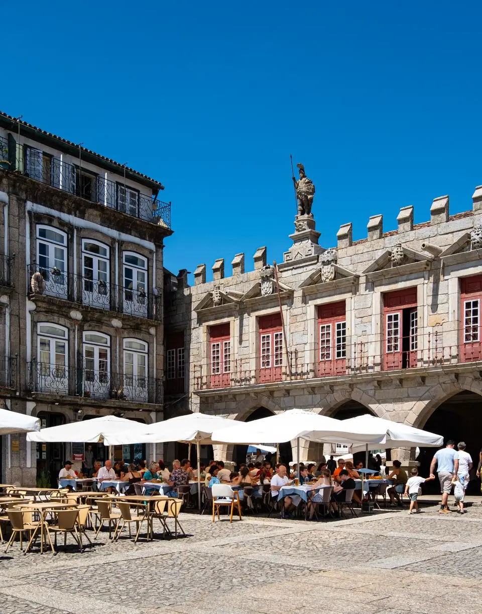 Lively outdoor café in a historic square of Guimaraes, Portugal, under a clear blue sky.