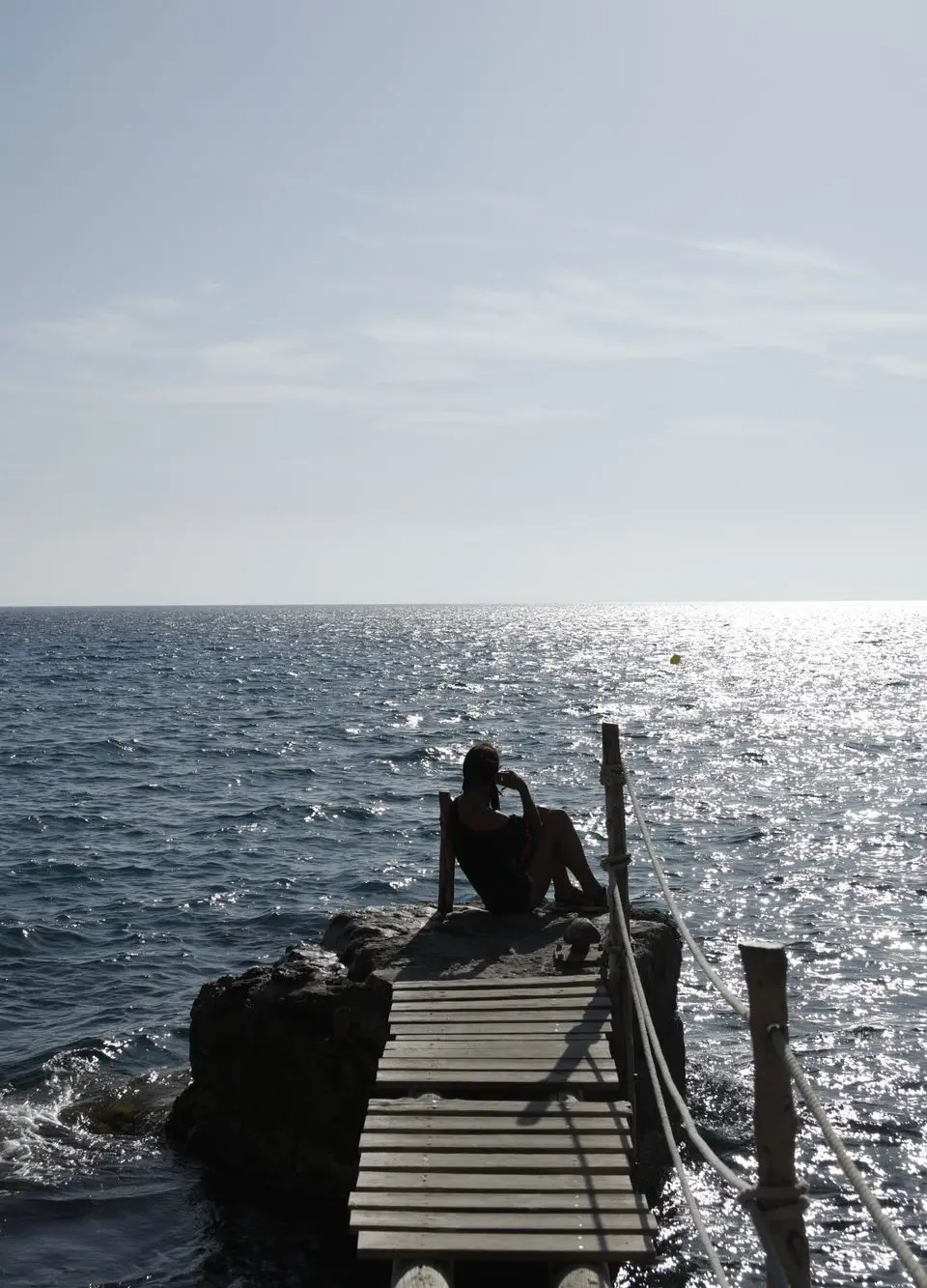 A tranquil silhouette on a wooden dock in Ibiza against a shimmering ocean sunset.