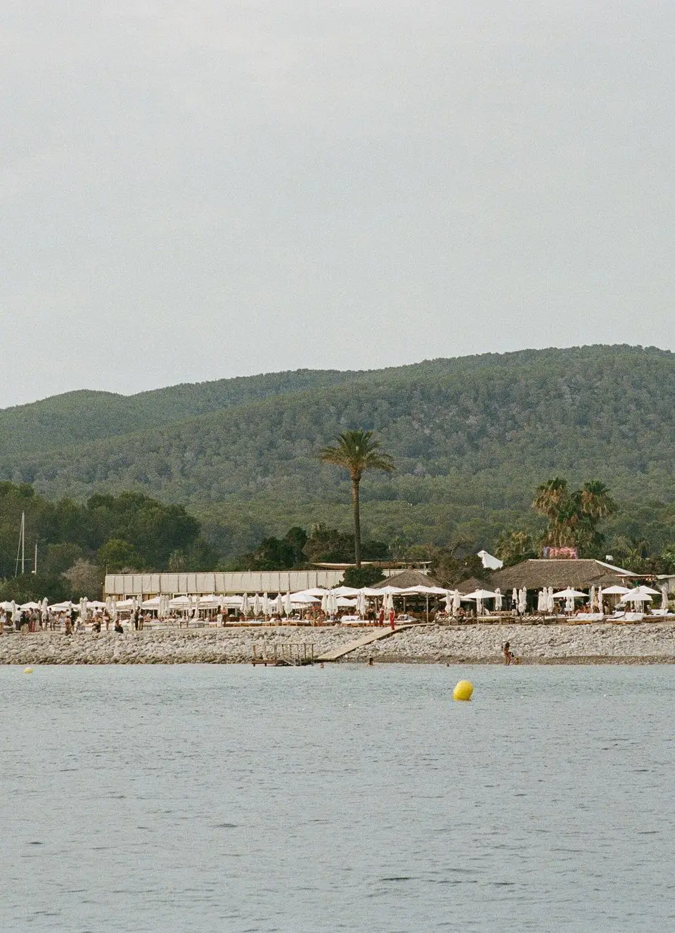 Serene beach scene in Eivissa with lush green hills and a distant resort.