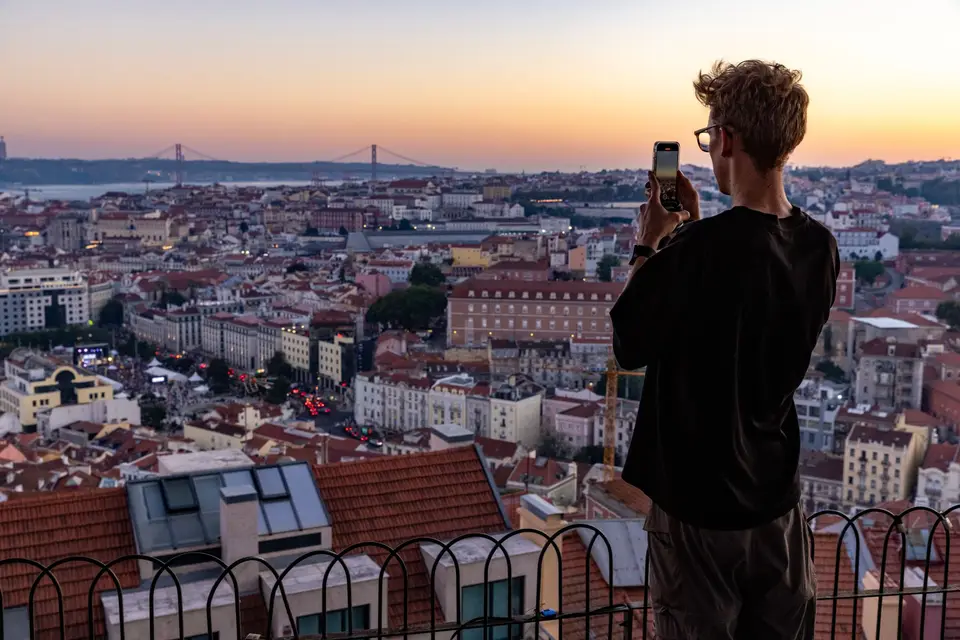 A man photographs the sunset over Lisbon, capturing its stunning cityscape from a high vantage point.