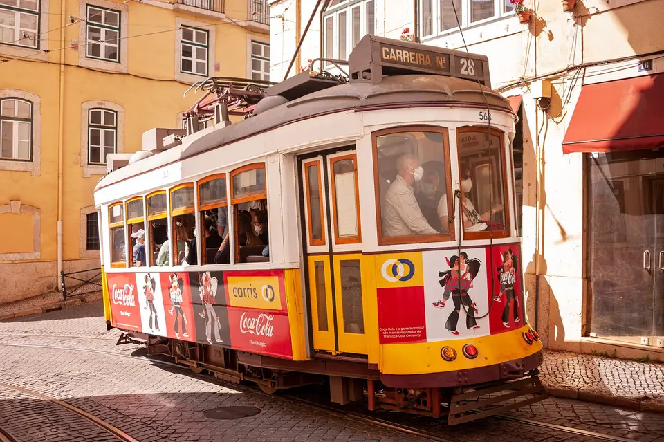 A vintage Lisbon tram with a Coca-Cola ad travels through sunny city streets, capturing urban travel charm.