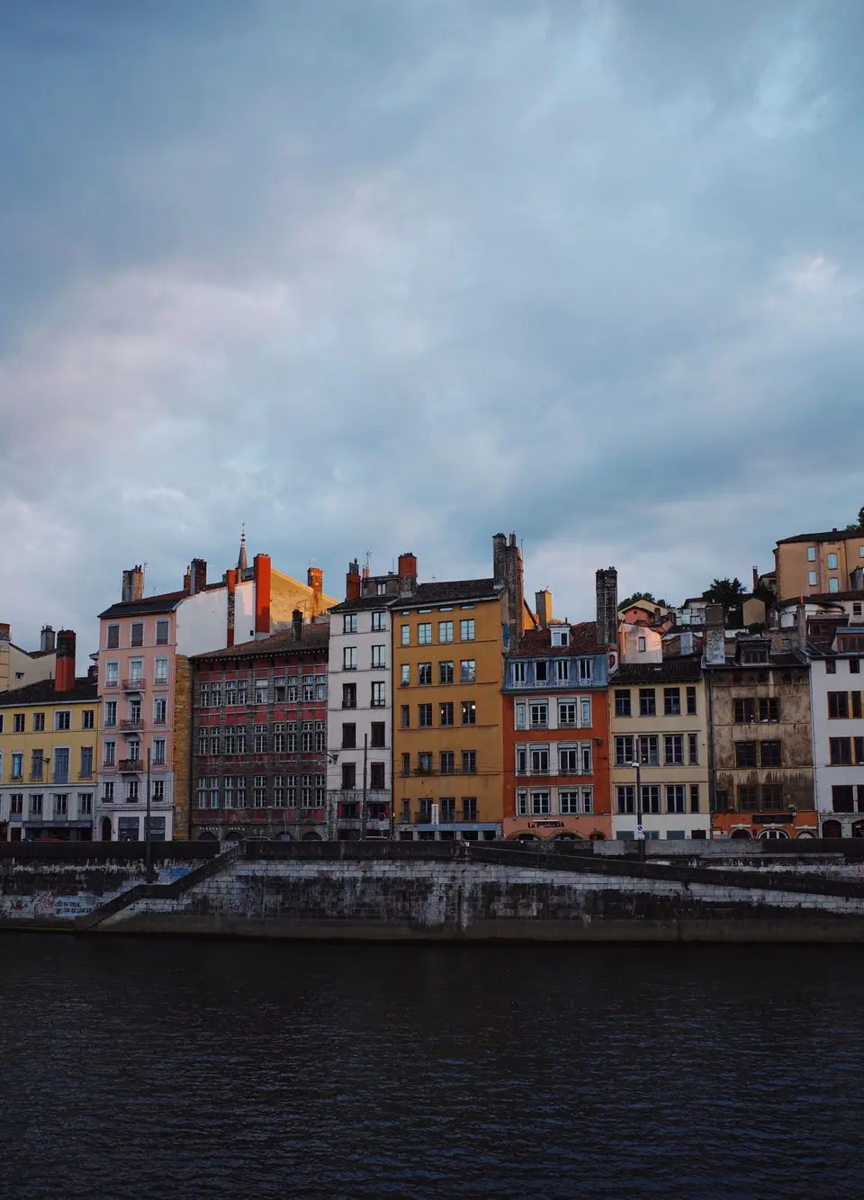 Charming view of Lyon's colorful terraced houses along the river under dramatic skies.
