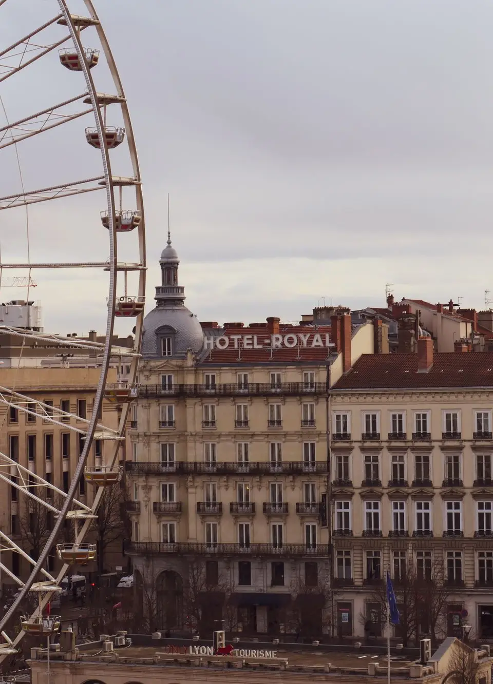 A scenic view of a Ferris wheel beside Hotel Royal in Lyon, France, showcasing classic architecture.