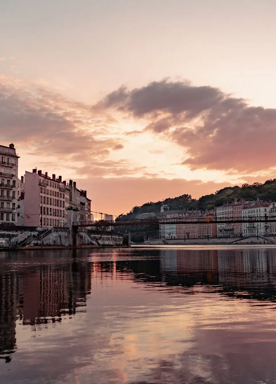 Beautiful sunset view over the Saone River in Lyon, France, showcasing urban townhouses and reflections.
