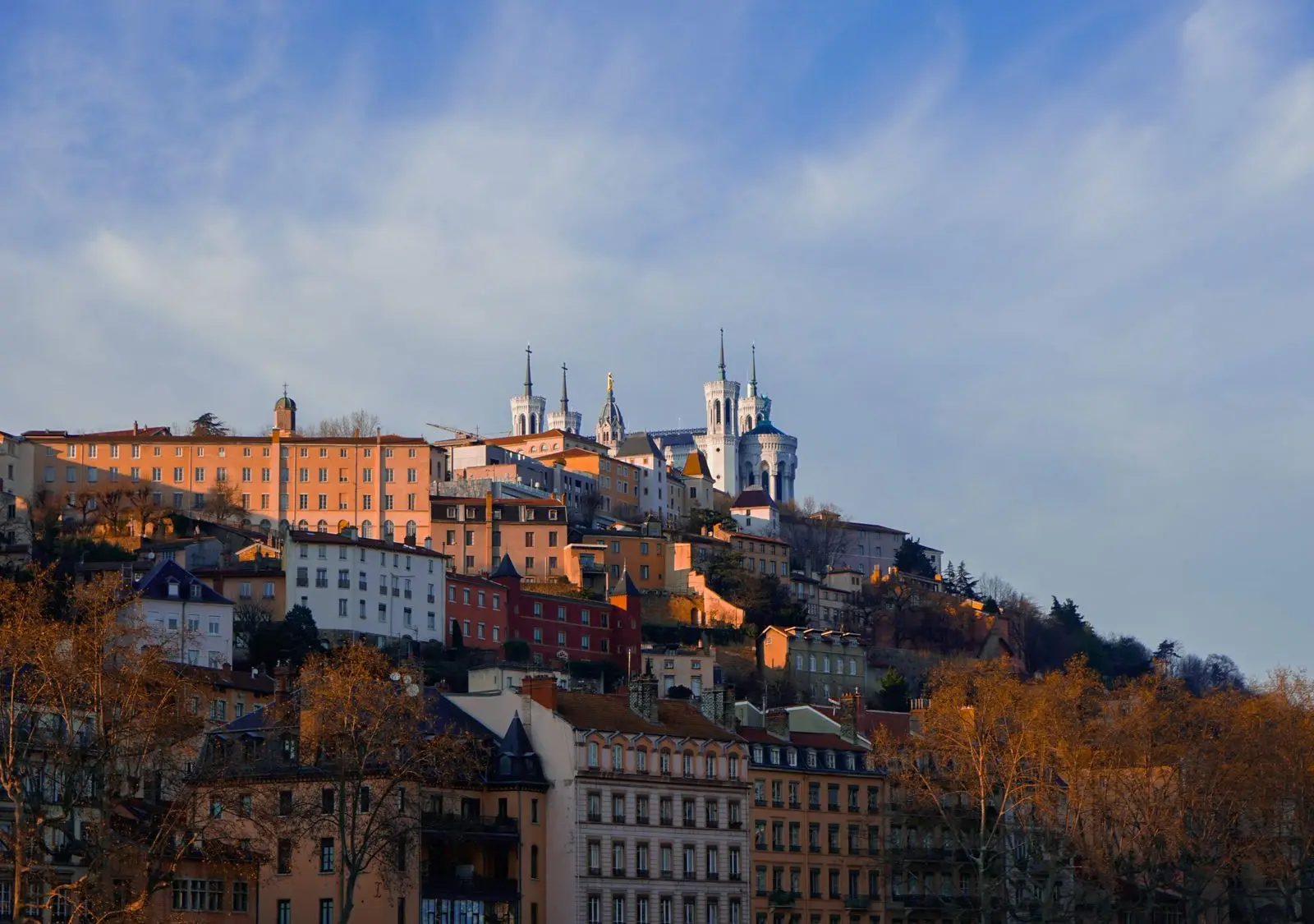 A scenic view of Lyon's historic old town and Basilica of Notre-Dame de Fourvière basking in the warm evening light.