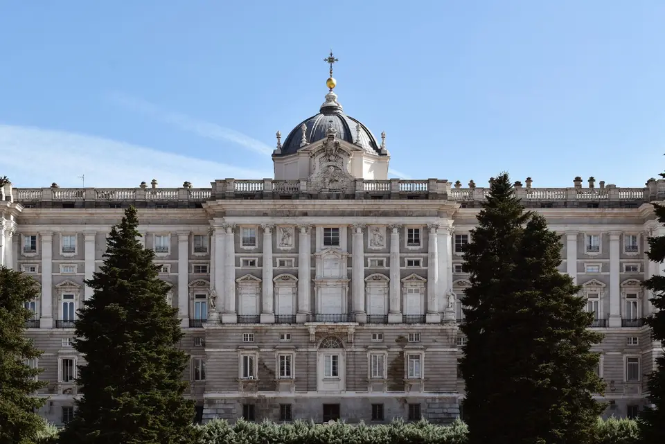 The grand facade of the Royal Palace of Madrid under a clear blue sky, framed by lush trees.