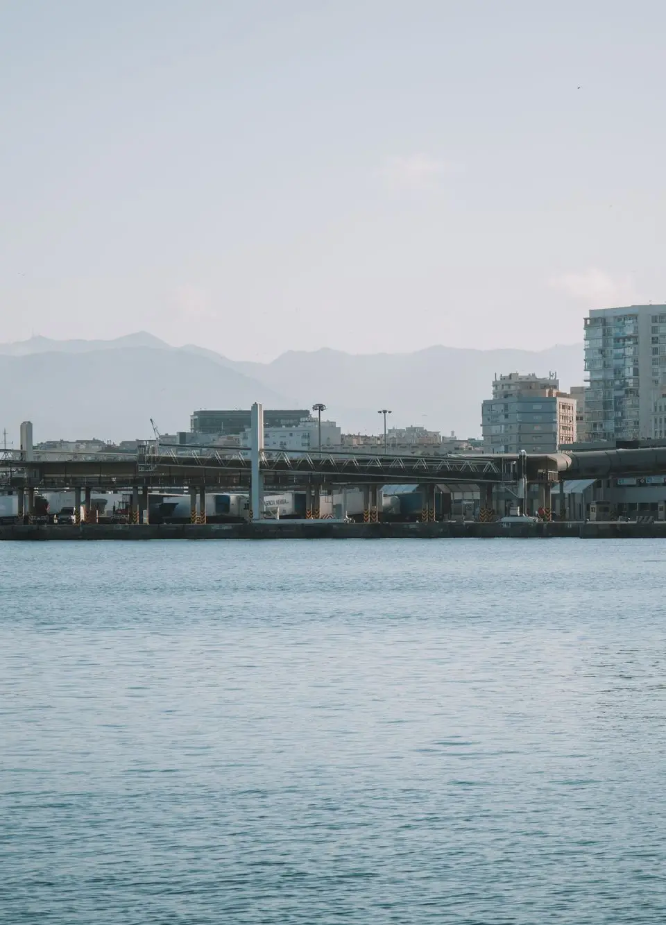 Scenic view of Málaga harbor with urban skyline and mountains in the background.