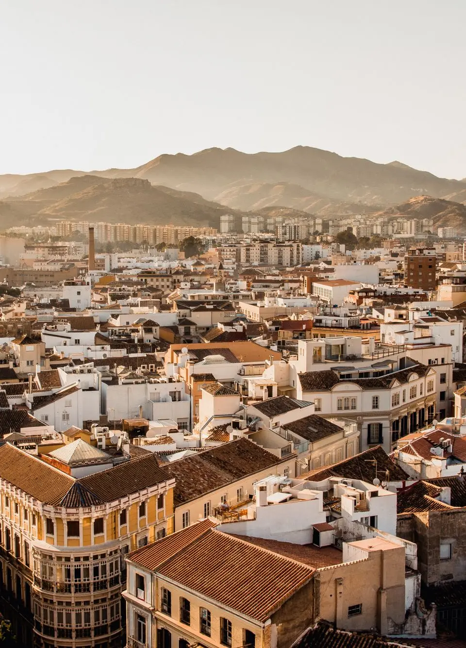 Aerial view of Málaga's cityscape with mountains in the background during sunset.
