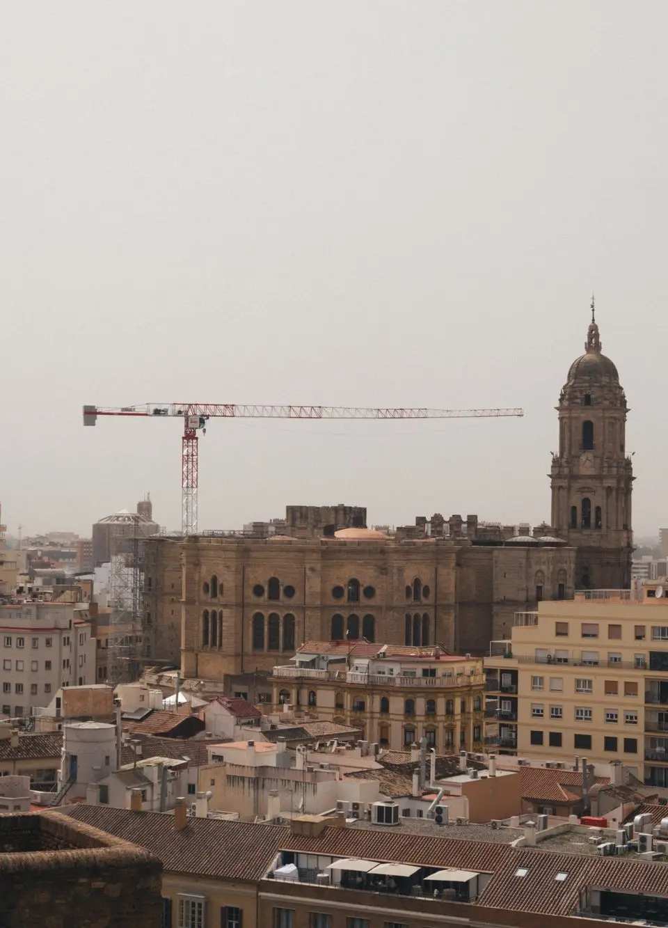 A stunning urban landscape featuring Malaga Cathedral amidst cranes and city buildings.