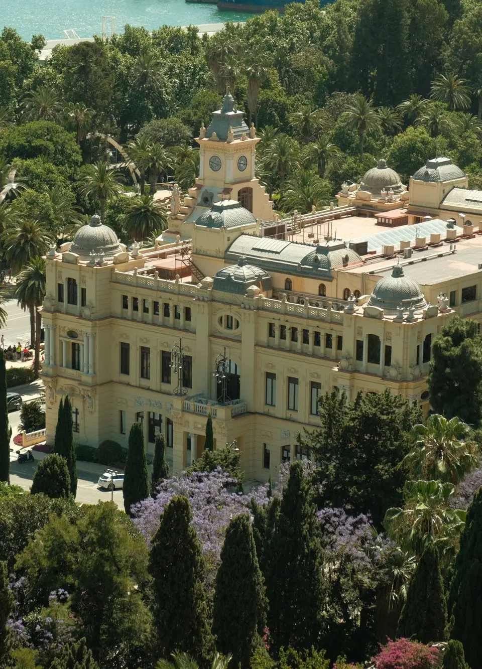 A picturesque aerial shot of Málaga City Hall, nestled among verdant trees with a coastal backdrop, in sunny Spain.