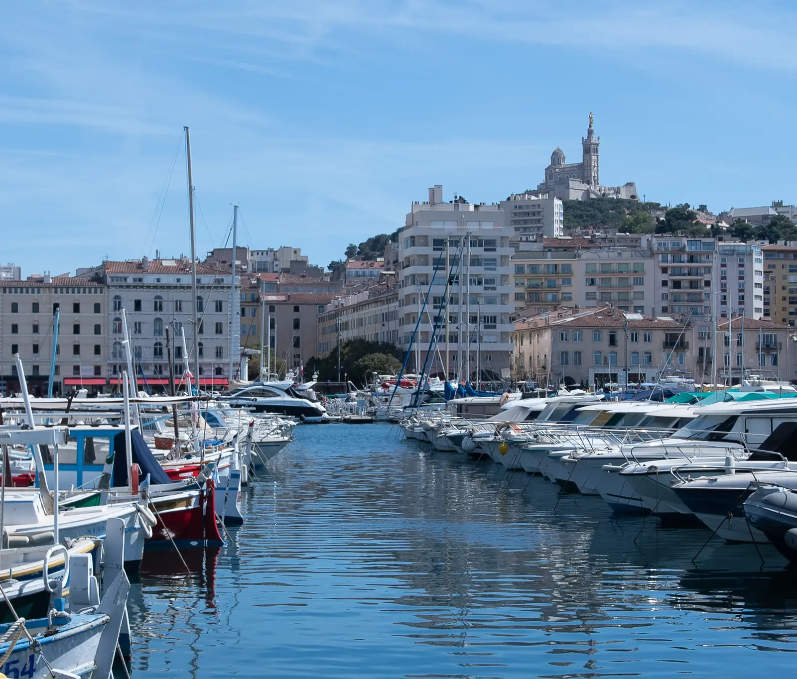 Explore the serene Marseille Vieux Port with yachts and a view of Notre-Dame de la Garde.
