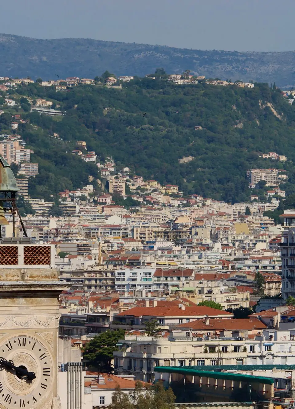 A stunning view of a historic clock tower with the cityscape of Nice, France in the background.