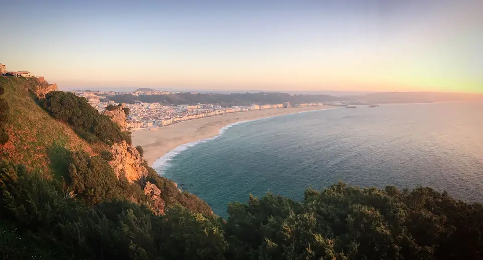 Breathtaking view of Nazare beach and coastline at sunset, capturing the village and ocean under a warm glow.