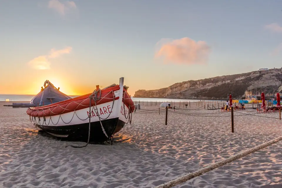Beautiful sunset beach view with a traditional red and white boat beached on the sand in Nazaré, Portugal.