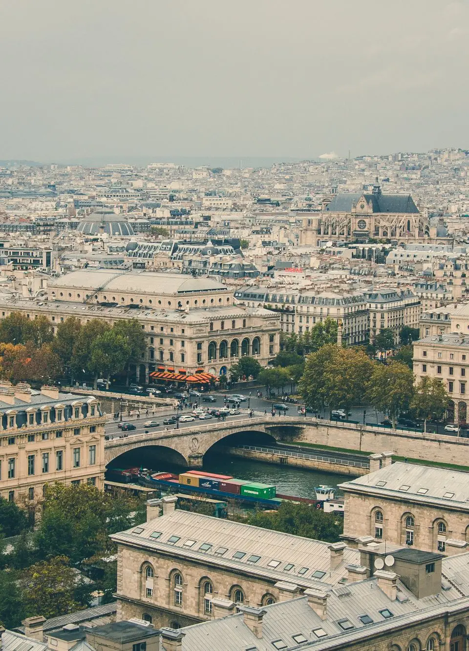 Aerial view of Paris cityscape featuring Seine River and historic architecture under a cloudy sky.