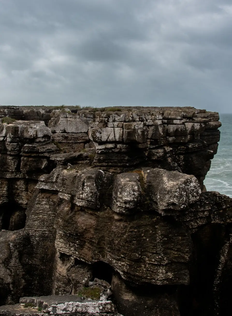 Scenic view of rugged cliffs meeting the Atlantic Ocean under a cloudy sky, Peniche, Portugal.