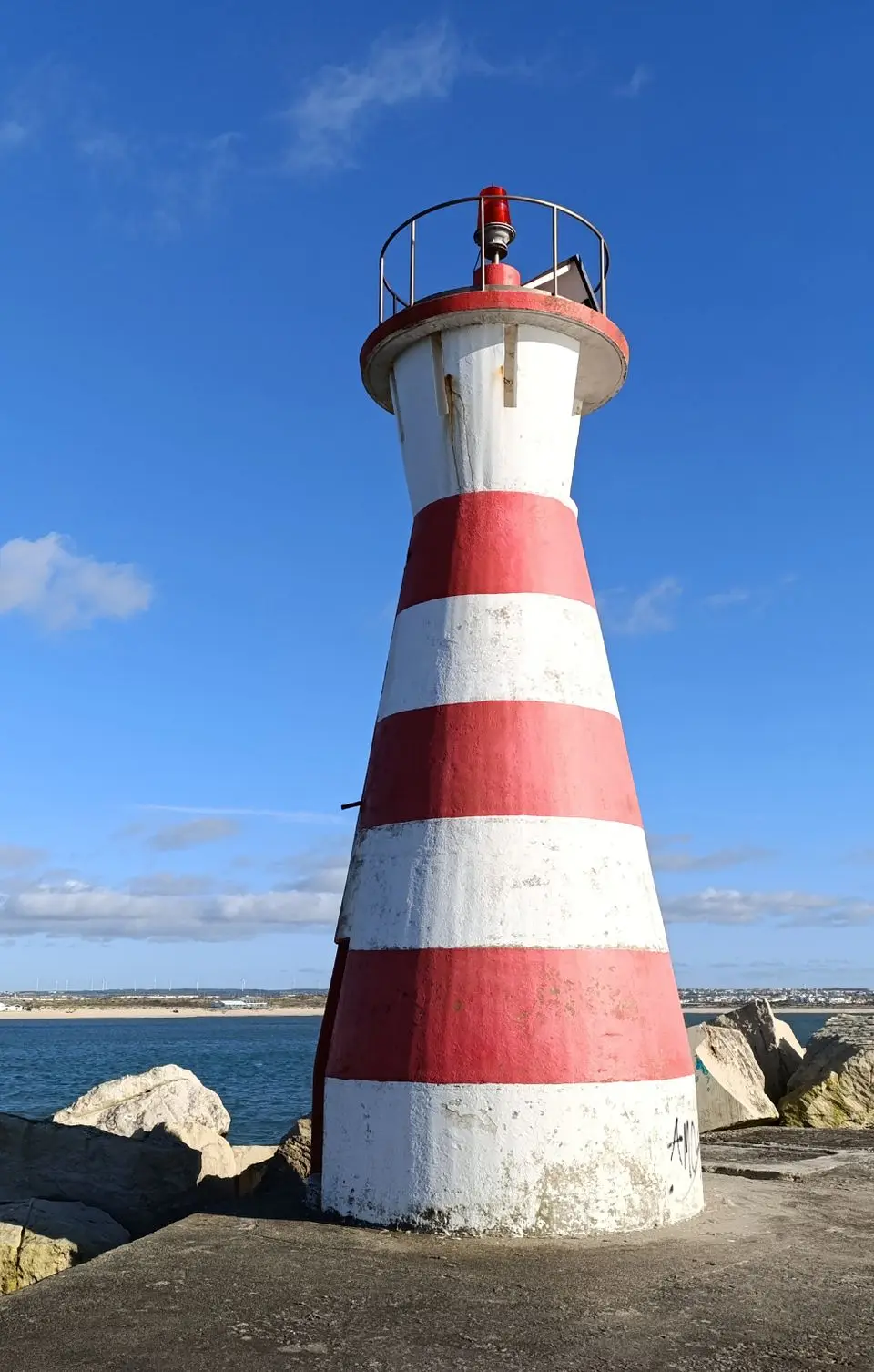 Vibrant red and white striped lighthouse on a rocky coast in Peniche, Portugal.