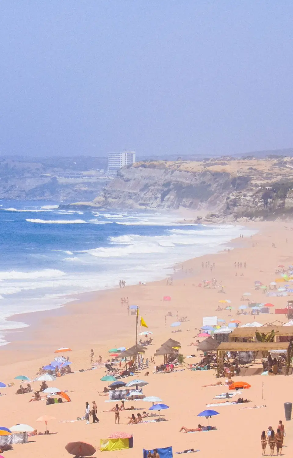 Sun-drenched beach in Peniche, Portugal, with colorful umbrellas and seaside cliffs.