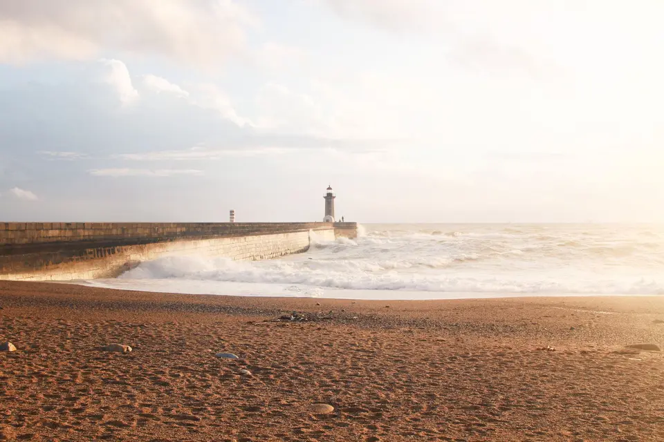 Captivating view of Porto's lighthouse by the ocean at sunset with waves crashing on the shore.